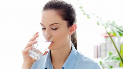 Młoda ciemnowłosa kobieta pije wodę ze szklanki