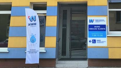 Wejście do budynku Biura Obsługi Klienta MWiK, obok biało niebieska flaga reklamowa