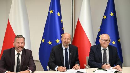 trzech biznesowo ubranych mężczyzn zasiada za stołem konferencyjnym uśmiechając się